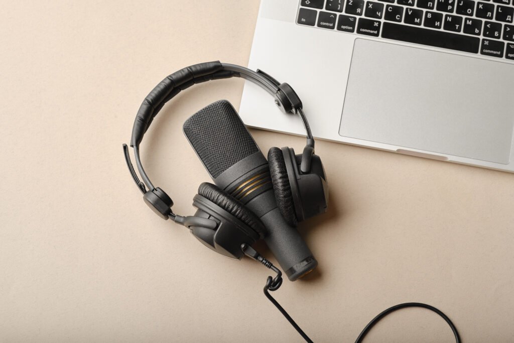 Microfone e fones de ouvido pretos sobre uma mesa clara, ao lado de um notebook prateado parcialmente visível.