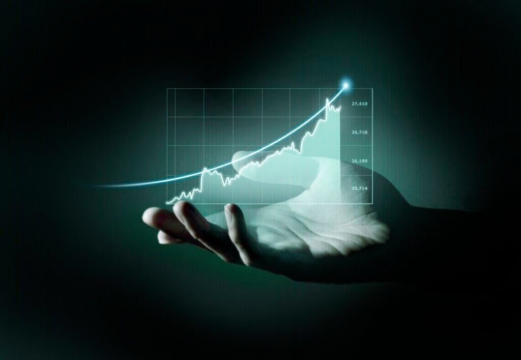 Mão aberta sustentando um gráfico holográfico de crescimento. A imagem mostra uma linha ascendente brilhante em azul-turquesa sobre uma grade com indicadores numéricos, simbolizando aumento de vendas, desempenho comercial e crescimento de resultados. O fundo escuro destaca o efeito tecnológico e futurista da projeção.