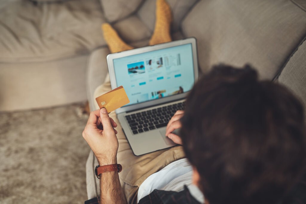 Pessoa utilizando um notebook para realizar compras online enquanto segura um cartão de crédito. A cena representa o comportamento do consumidor digital, decisões de compra e o crescimento do comércio eletrônico.