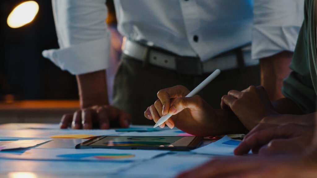 Equipe reunida em ambiente corporativo analisando dados e gráficos em um tablet durante uma reunião estratégica. Profissionais utilizam recursos digitais para avaliar métricas, planejar ações e desenvolver estratégias de marketing industrial voltadas para crescimento, posicionamento de marca e geração de oportunidades de negócio.