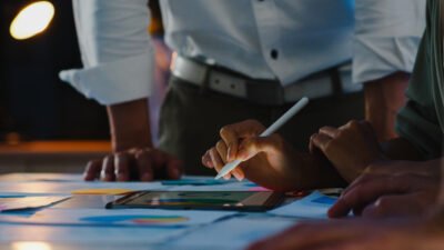 Equipe reunida em ambiente corporativo analisando dados e gráficos em um tablet durante uma reunião estratégica. Profissionais utilizam recursos digitais para avaliar métricas, planejar ações e desenvolver estratégias de marketing industrial voltadas para crescimento, posicionamento de marca e geração de oportunidades de negócio.