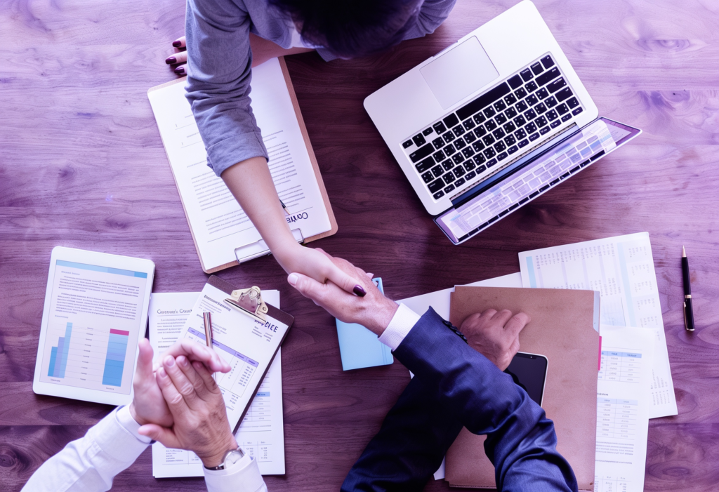 Business professionals shaking hands across a meeting table with laptops, financial reports, and documents, representing B2B partnerships, strategic collaboration, and business growth in Brazil.
